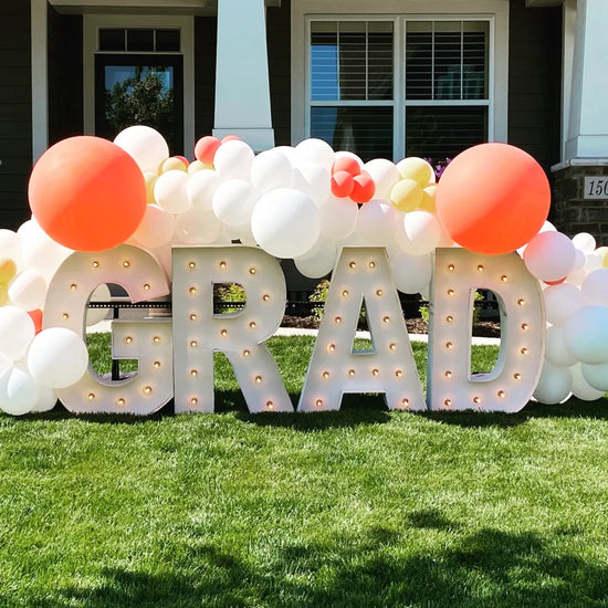 white and orange balloons surrounded the word grad